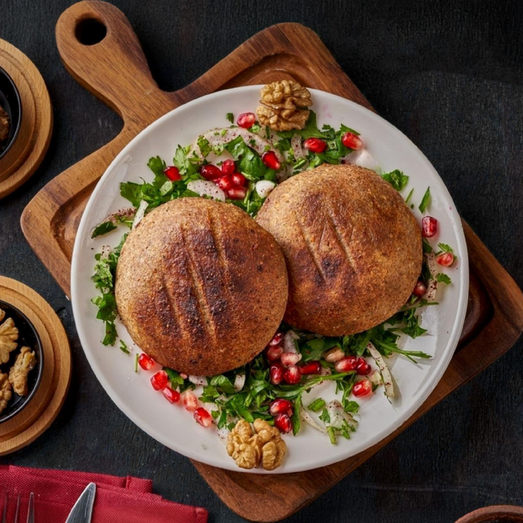 White plate with grilled kibbeh and pomegranate seeds on a dark background