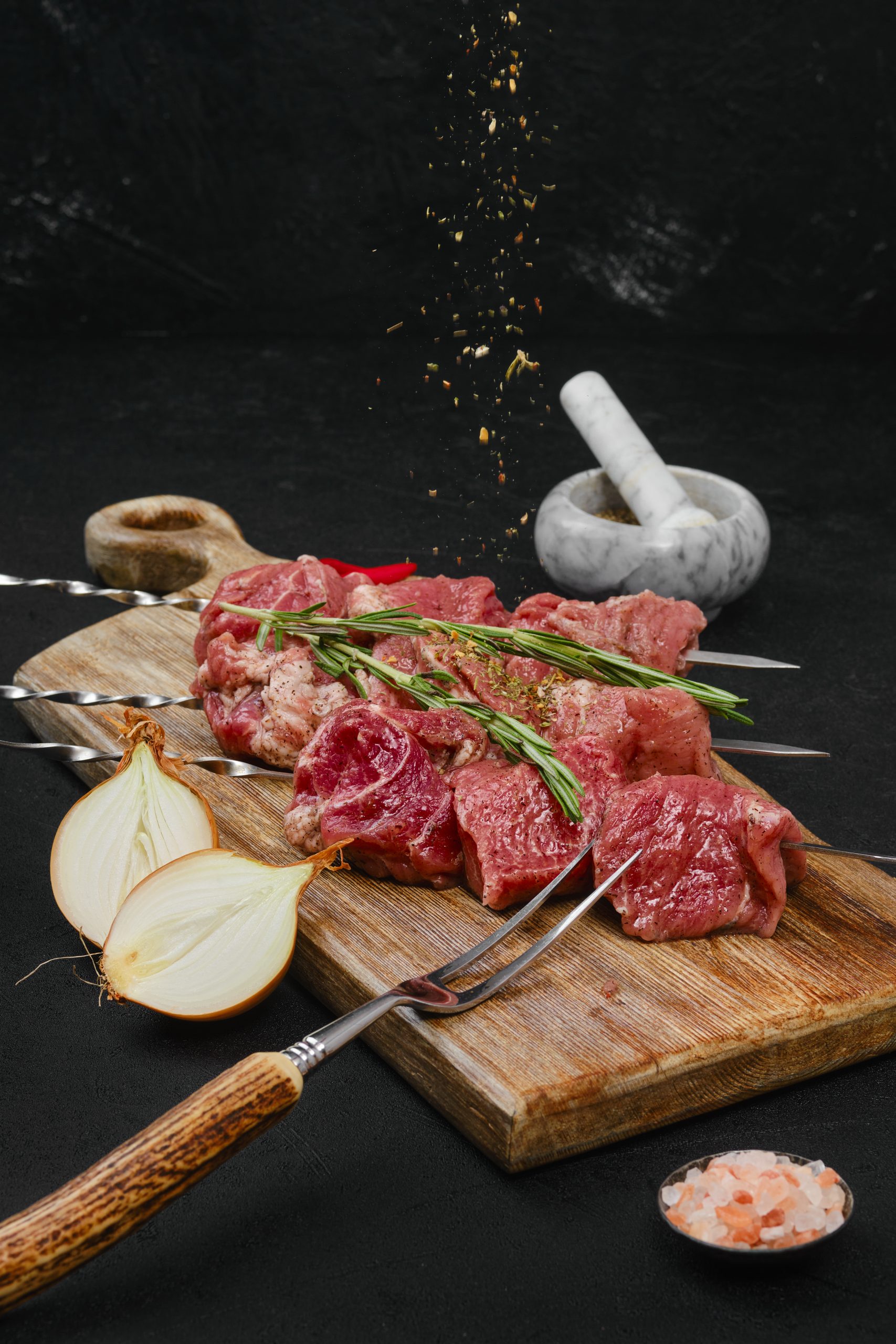 Sprinkling with spice raw beef meat on skewer