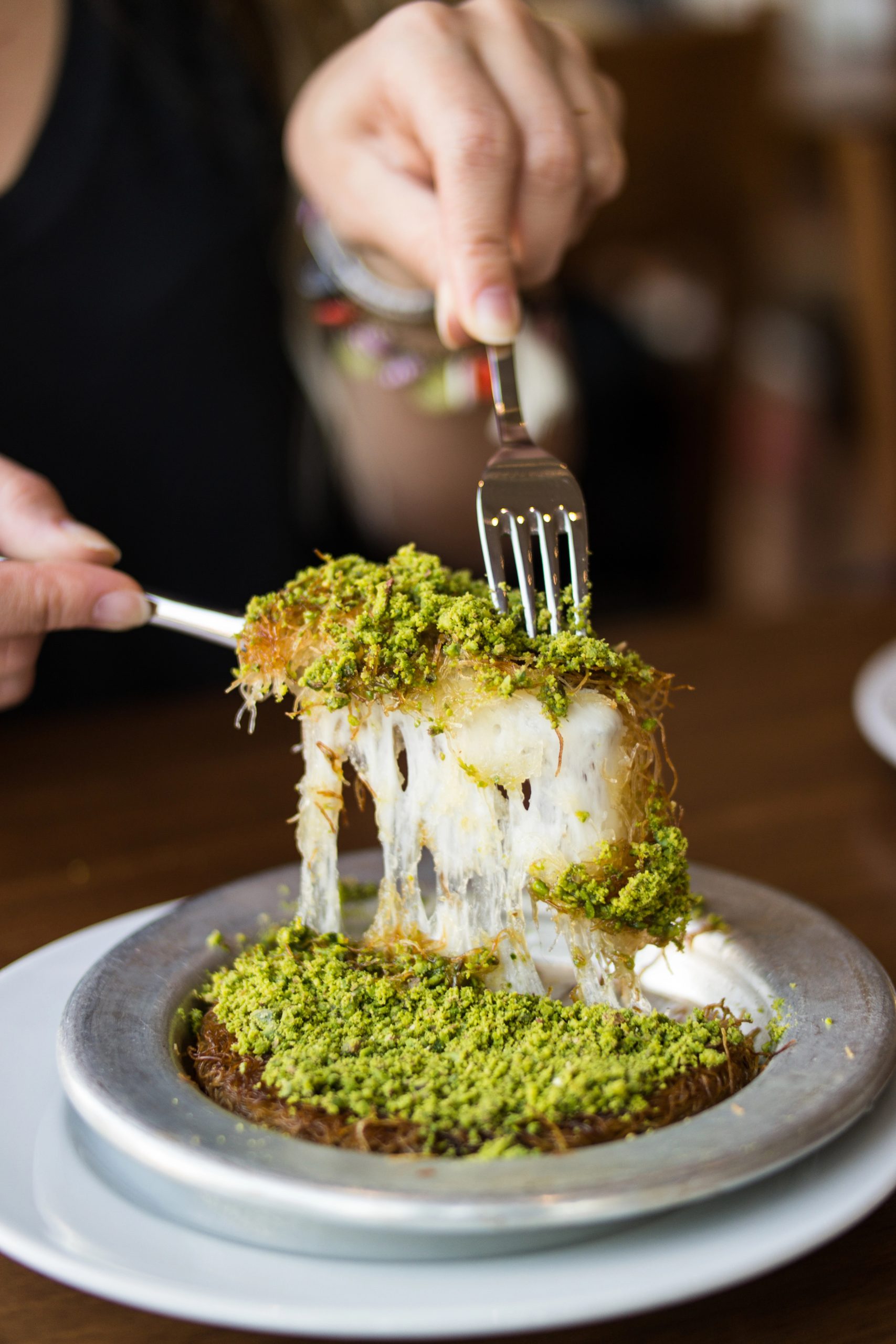 A woman cuts kunafa topped with green pistachios at Ottawa Kebab