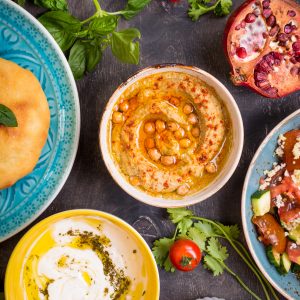 Table serving Middle Eastern vegetarian dishes, hummus, pomegranate, tahini, top view