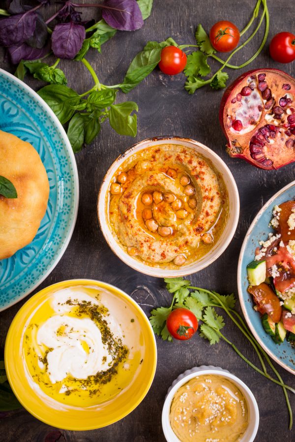 Table serving Middle Eastern vegetarian dishes, hummus, pomegranate, tahini, top view