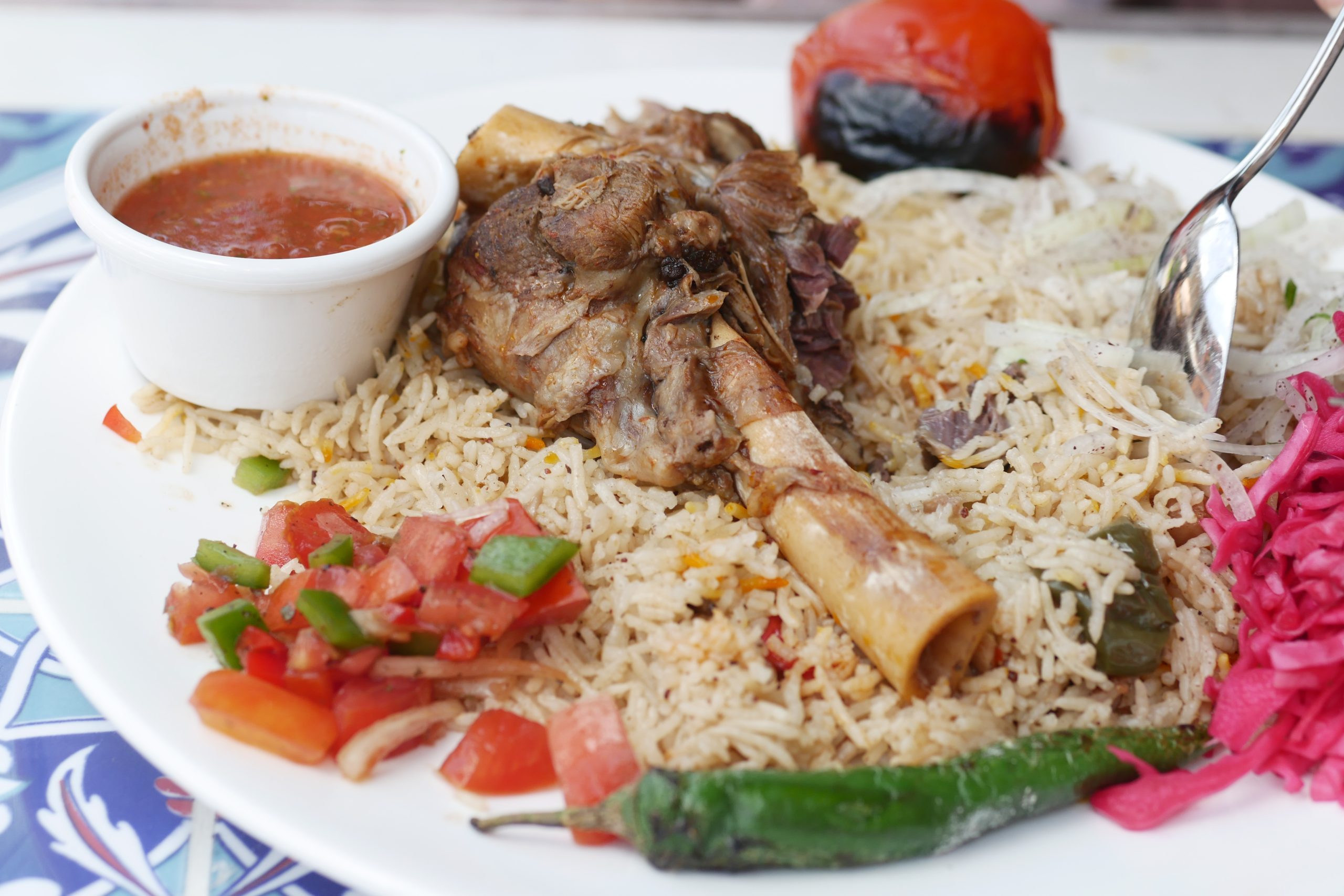 A white plate with rice and meat on top , Grilled tomatoes salad ,sauce